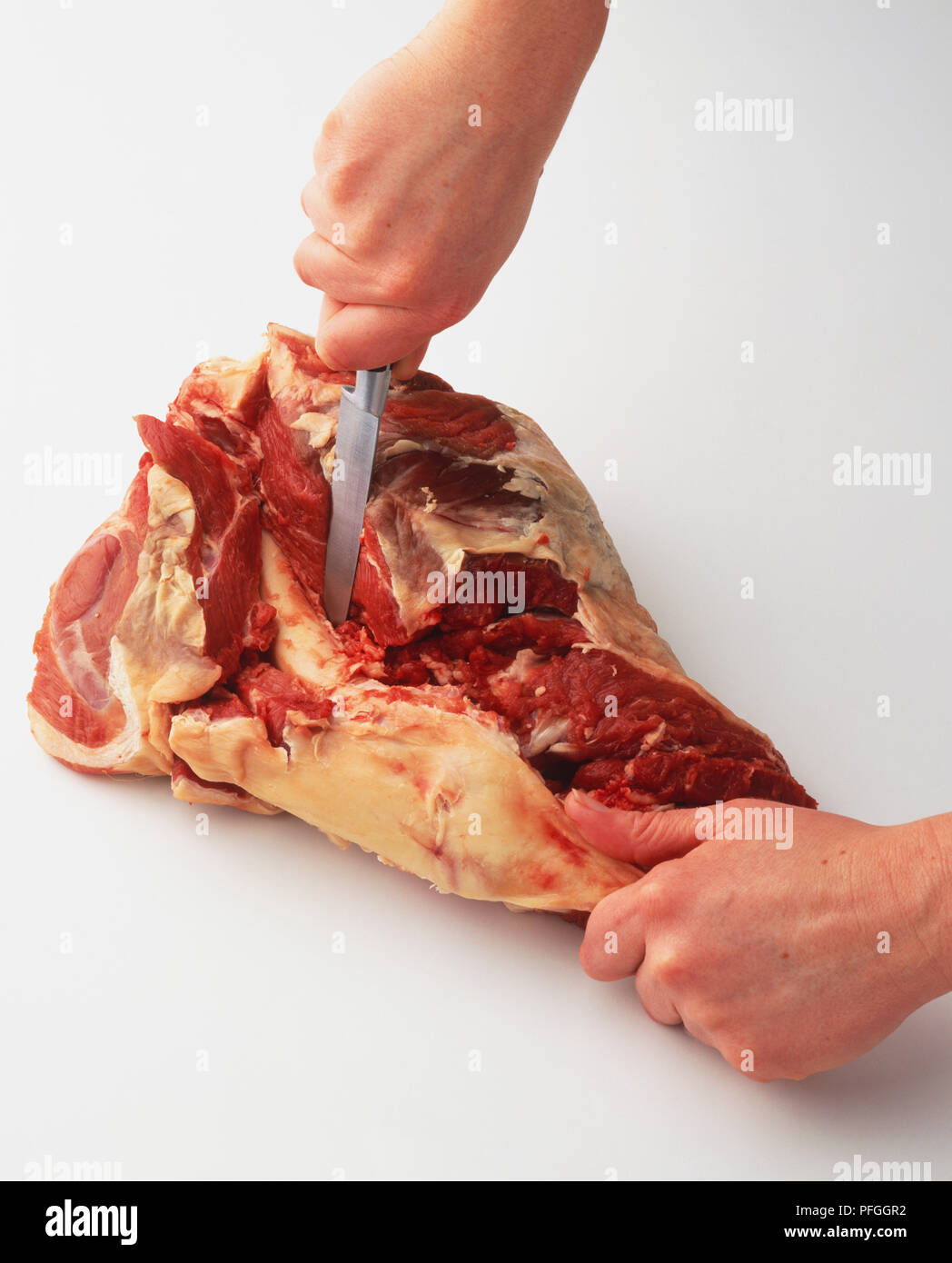Raw lamb meat being scraped away from the leg bone with knife, view from above. Stock Photo