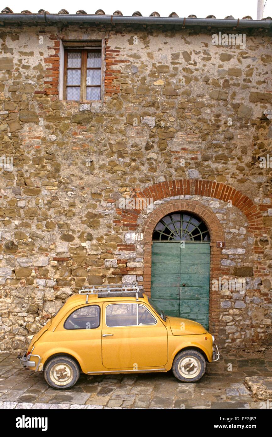 Italy, Tuscany, yellow Fiat 500 parked outside entrance to old stone house, close-up Stock Photo