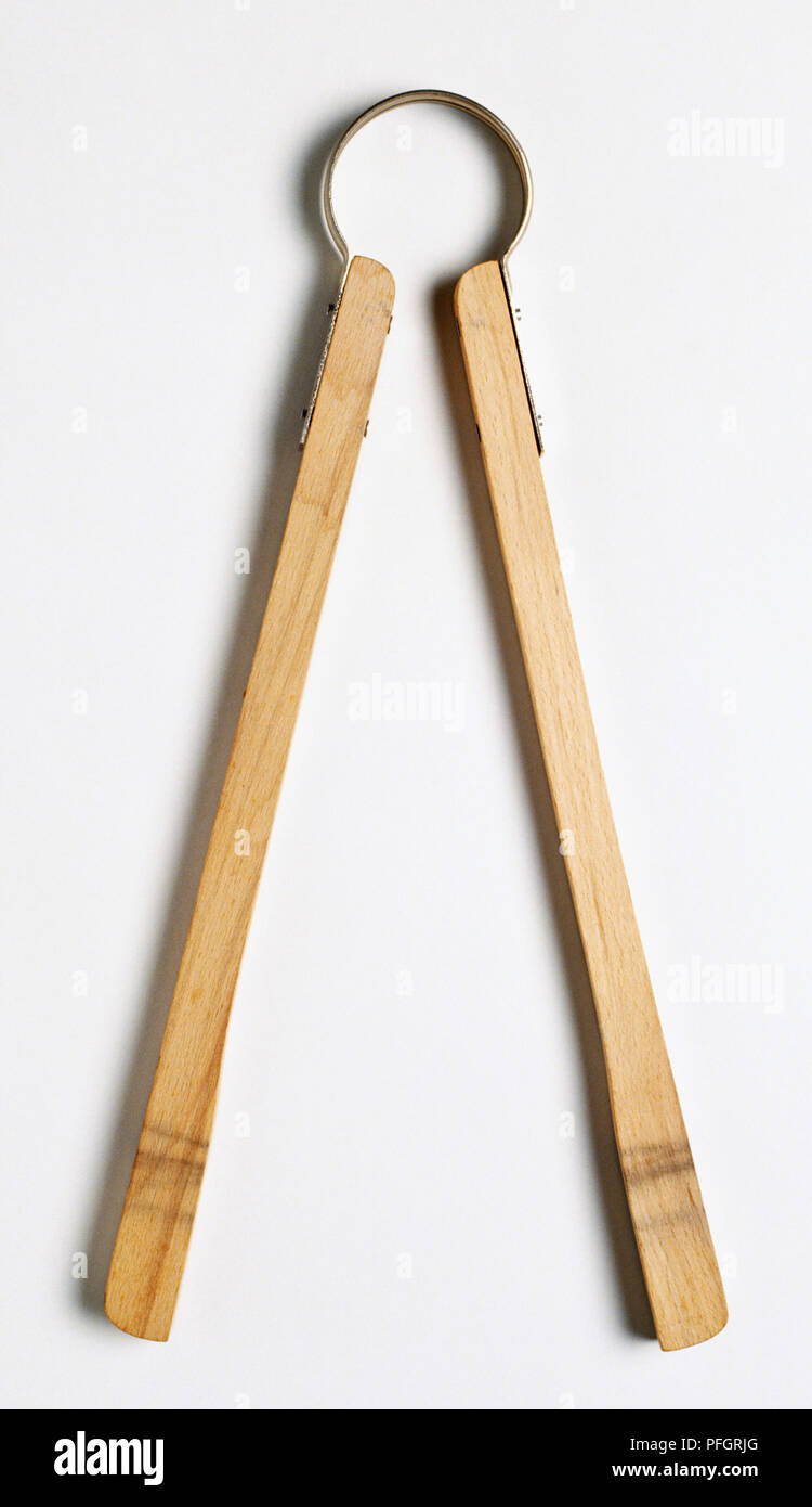 Metal kitchen thongs on wooden board Stock Photo - Alamy