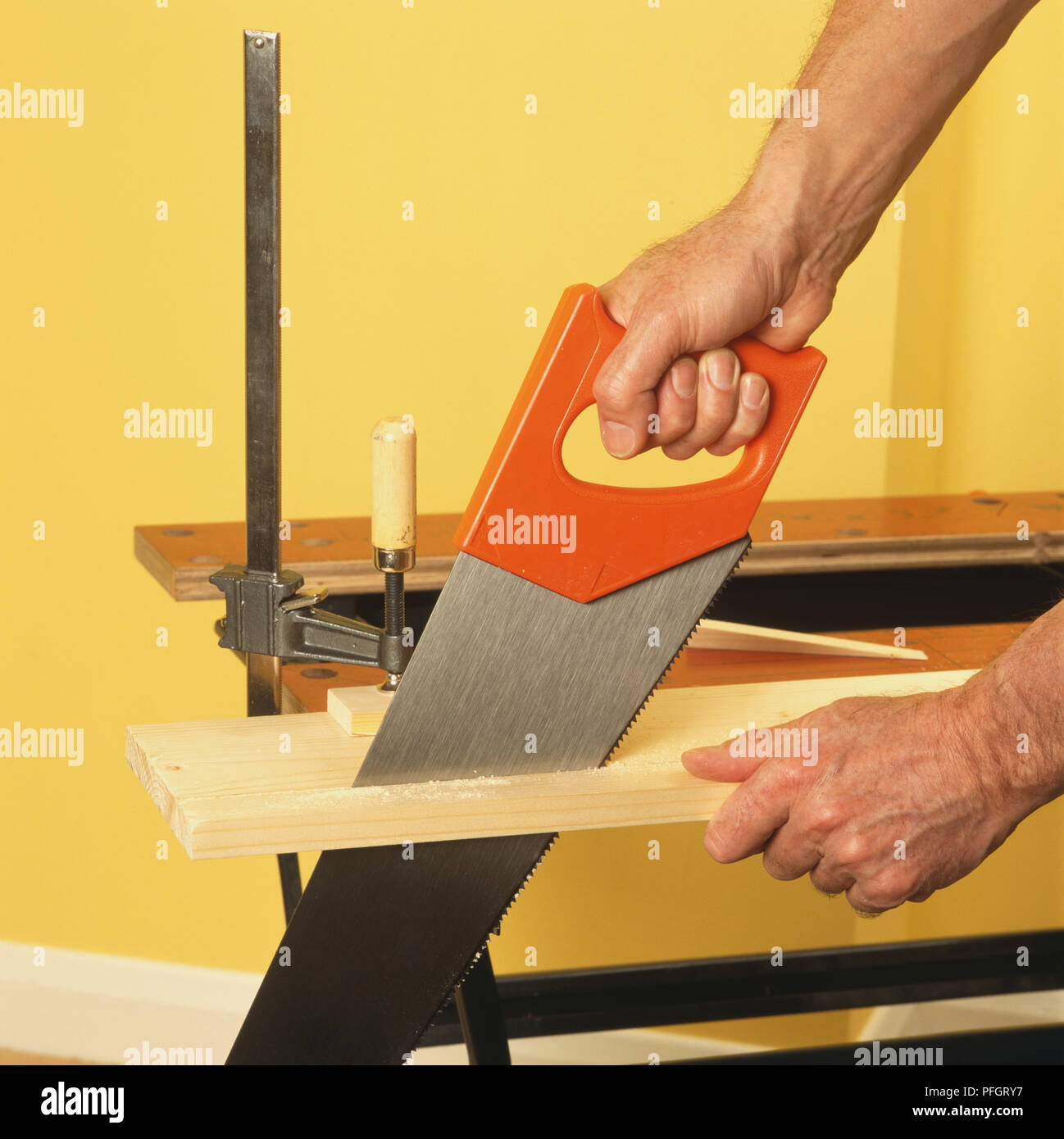 Hand Sawing Through A Plank Of Wood Clamped To A Work Bench Side