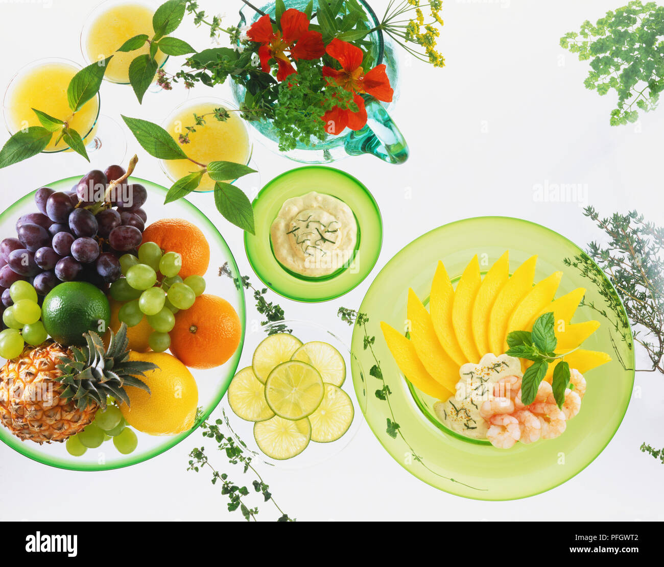 Bowls of fresh fruit, lime slices, herbs and dips, and a dish of sliced mango and peeled prawns Stock Photo