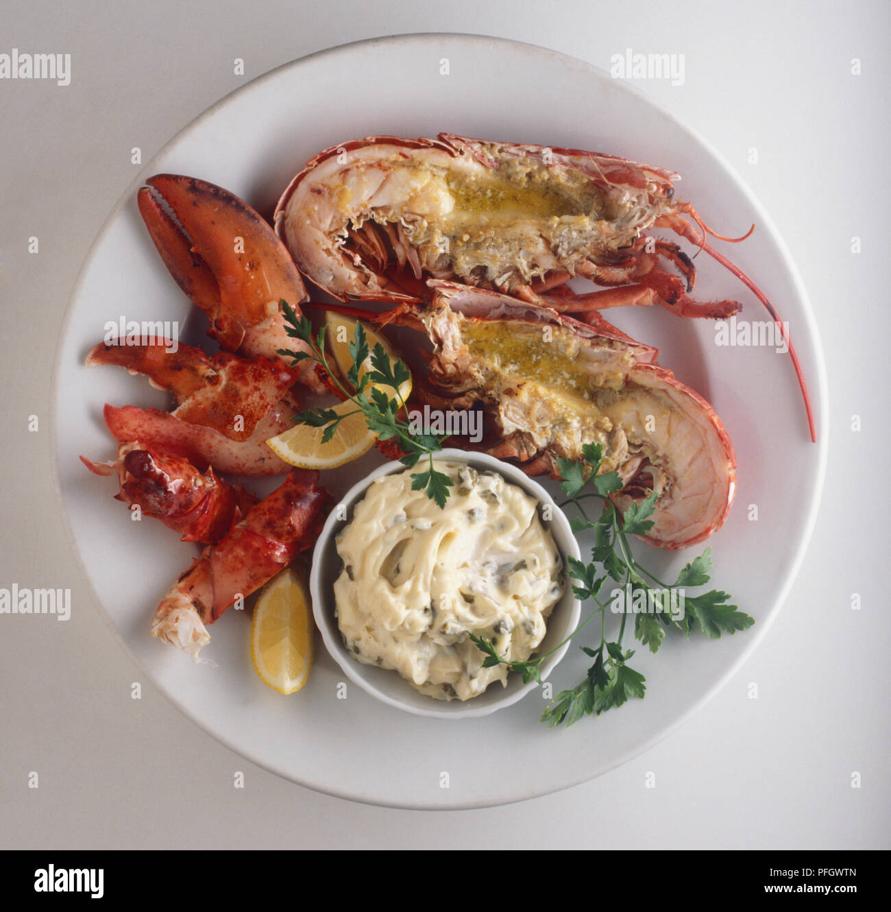 Langosta a la parrilla, lobsters served with bowl of mayonnaise, lemon slices and herbs, view from above Stock Photo