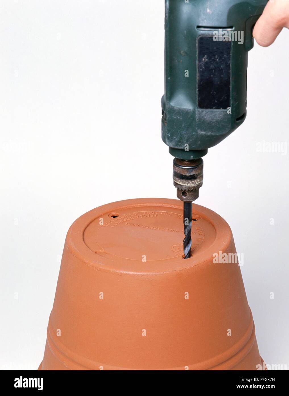 Using drill to make holes in base of upside down plant pot Stock Photo