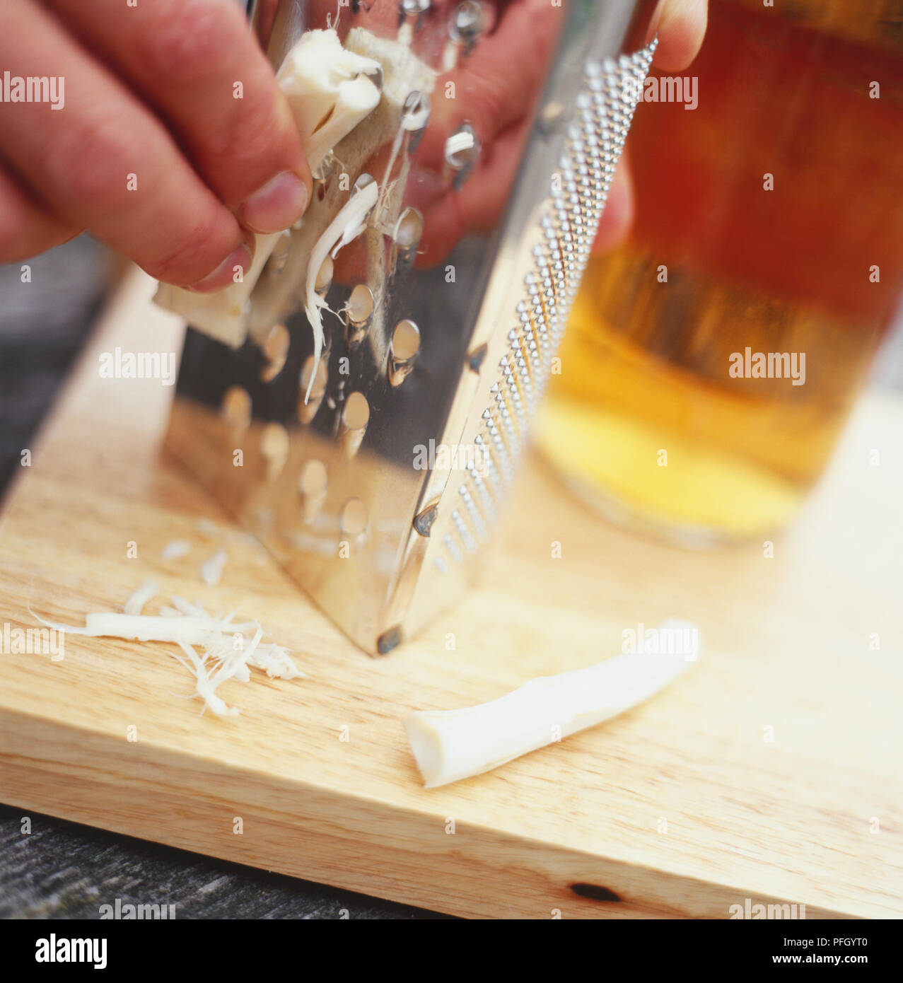 Grating horseradish root onto wooden chopping board, closeup Stock