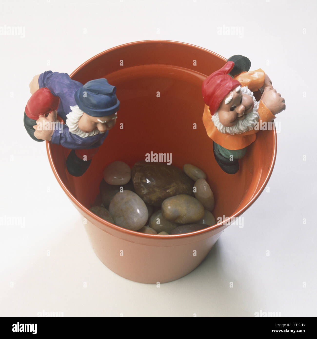 Two garden gnomes climbing inside edges of plastic plant pot, grey