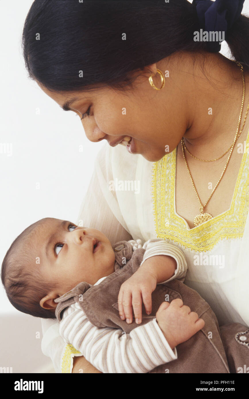 Black-haired woman cradling baby, looking at each other Stock Photo