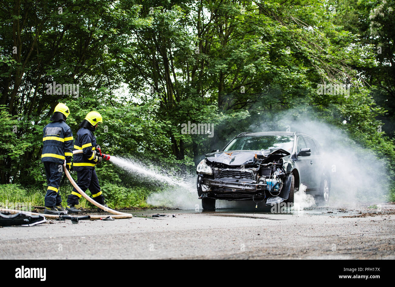 Two firefighters extinguishing a burning car after an accident on the ...