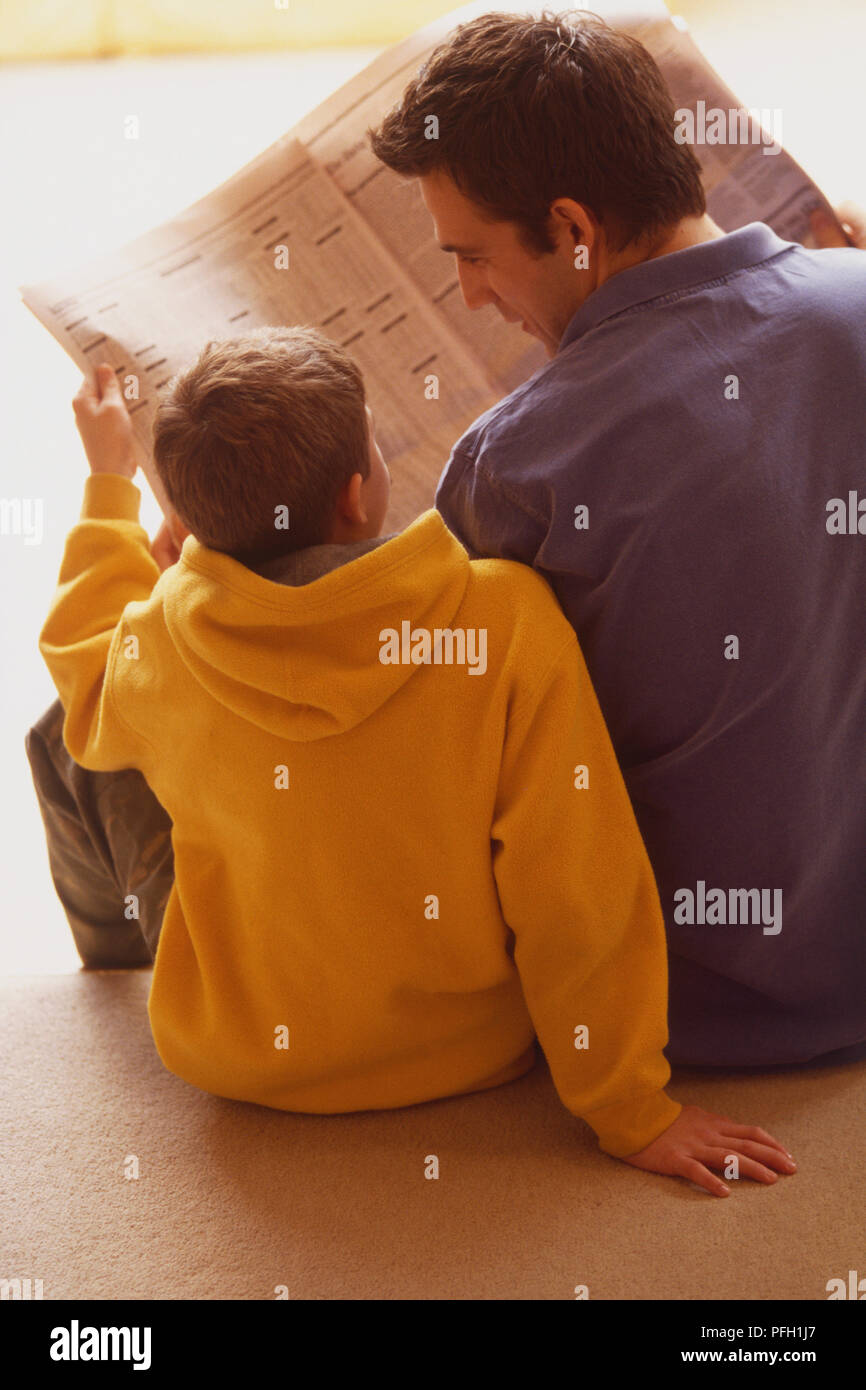Man sitting beside a boy on the floor, rear view Stock Photo