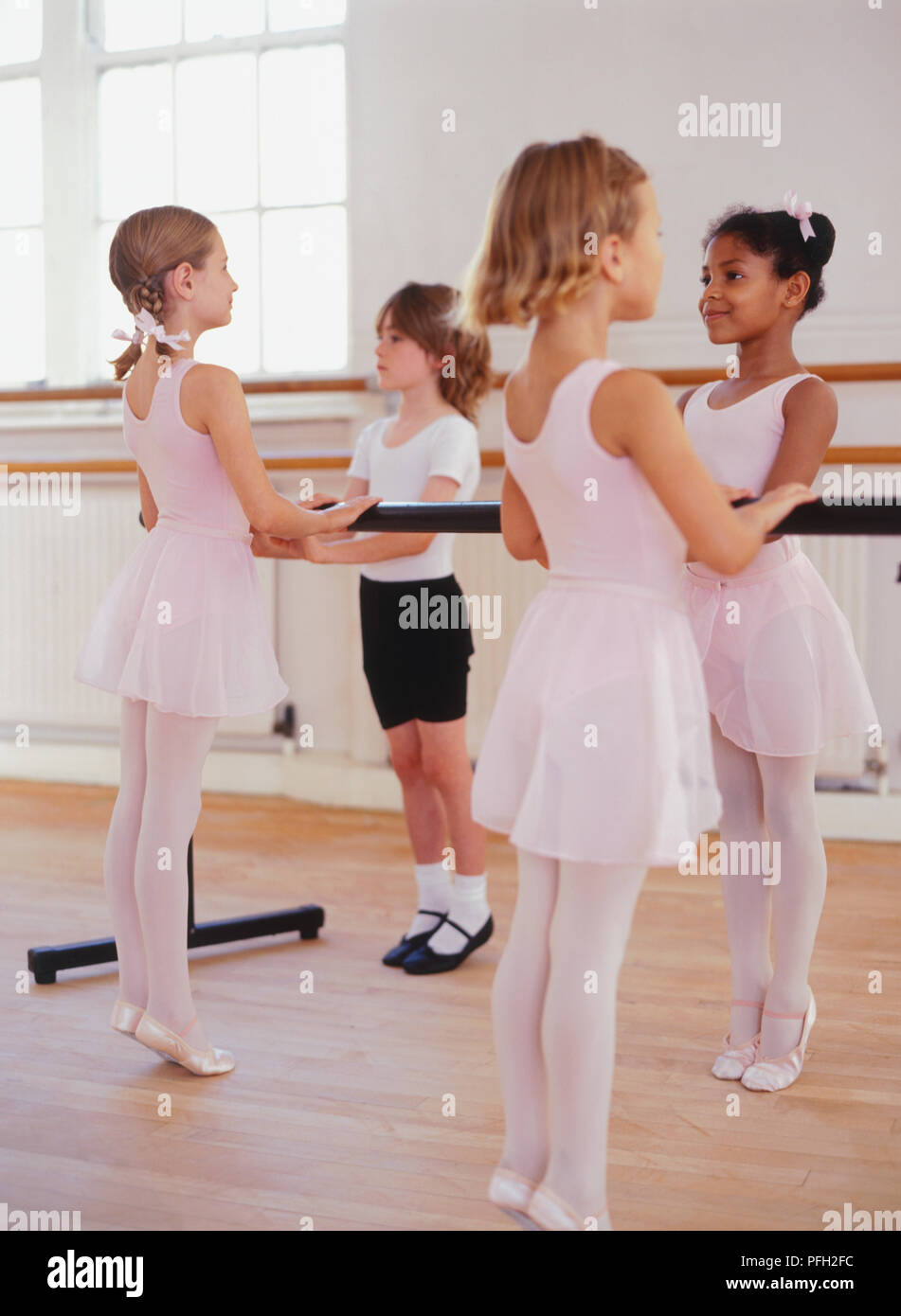 Four ballet dancers standing holding the barre on tip toes in a ballet