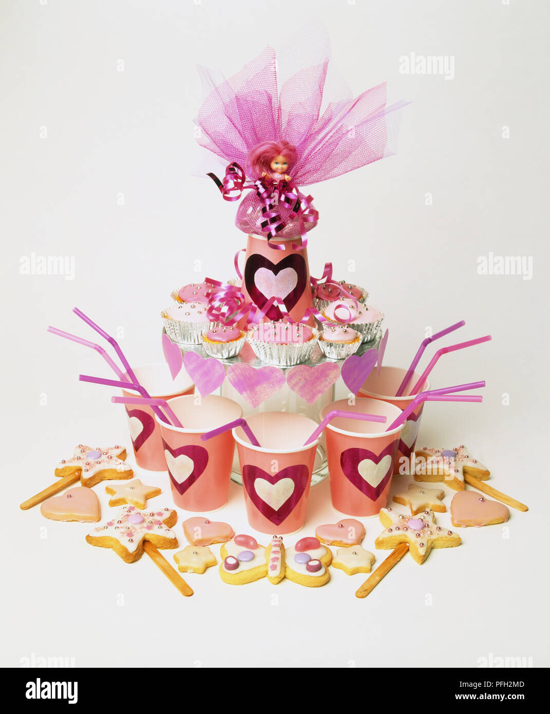 Girls' party pink table design, doll surrounded by fairy cakes, paper cups and decorated biscuits. Stock Photo