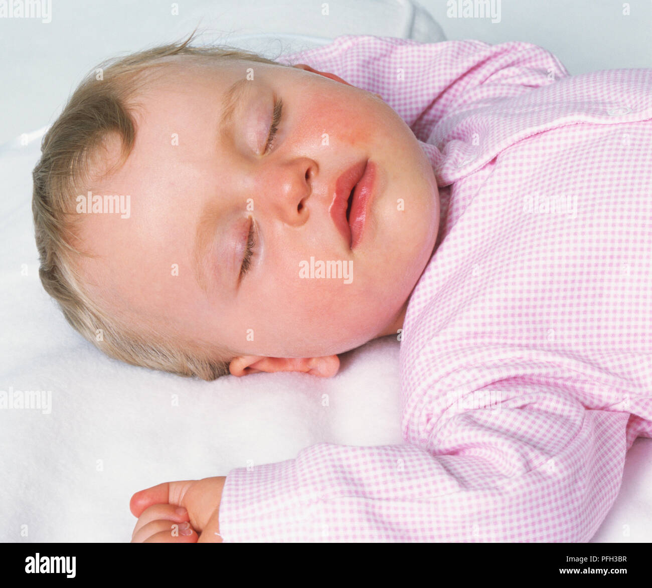 Head of baby girl sleeping on her back with her arms bent up by the