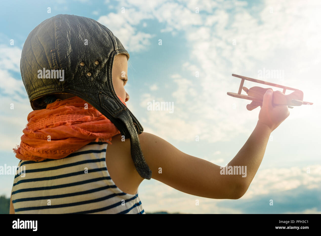 Happy kid playing with wooden toy airplane against blue summer sky ...