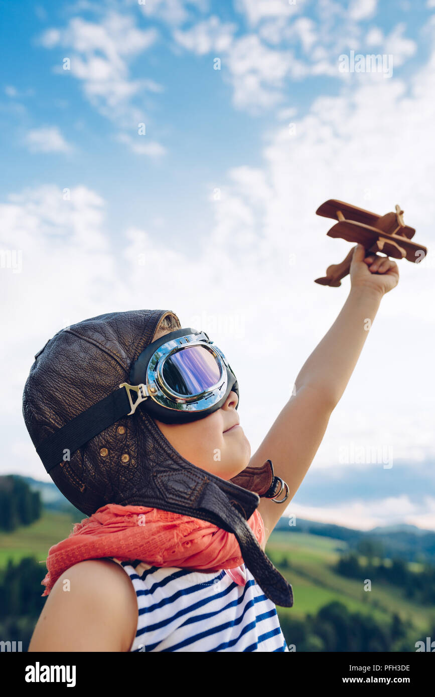 Happy kid playing with wooden toy airplane against blue summer sky ...