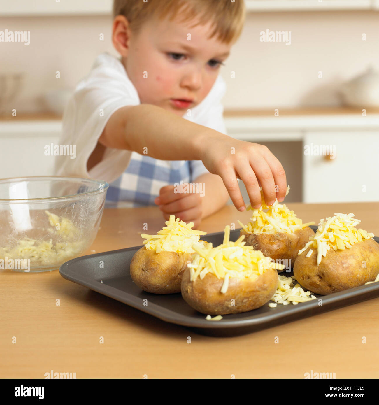 Boy placing cheese on jacket potato Stock Photo Alamy