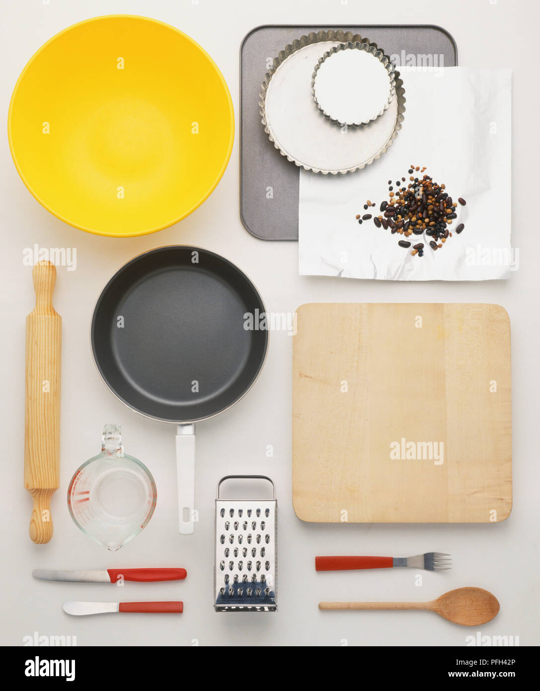 Array of baking and cooking utensils, including rolling pin, baking tins, bowls, frying pan, wooden cutting board, metal grater, measuring jug, knives and foil Stock Photo