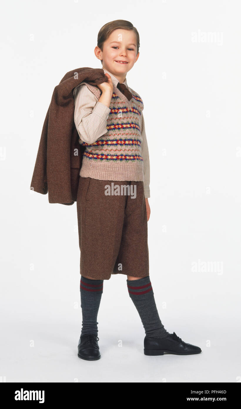 Boy in knitted pullover, brown knee-length trousers and a matching jacket over his shoulder, smiling and looking at camera Stock Photo