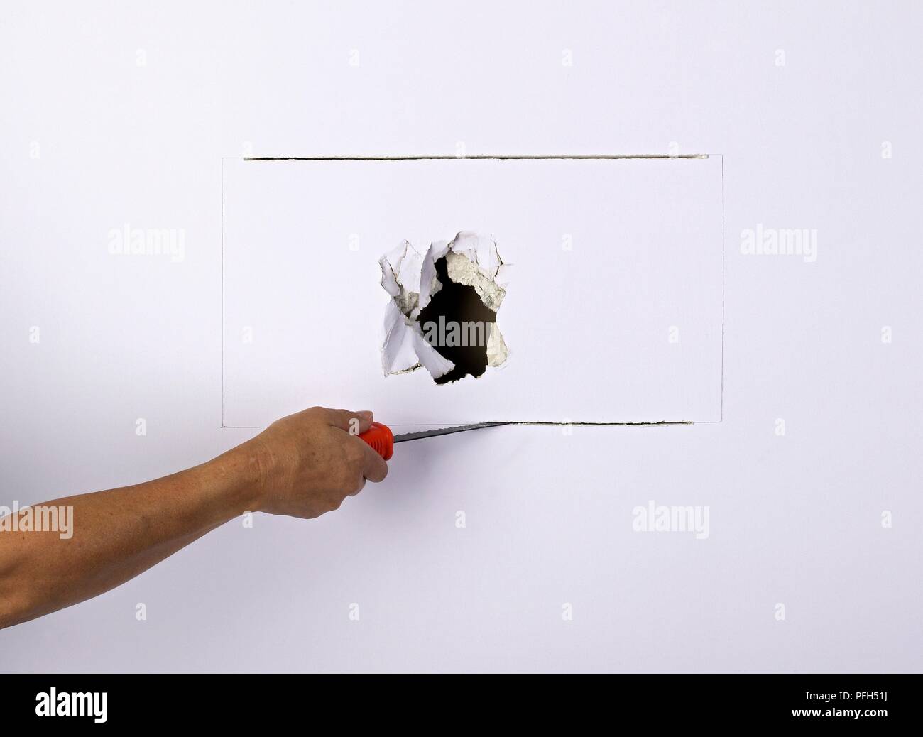 Hand cutting out section of damaged wall Stock Photo