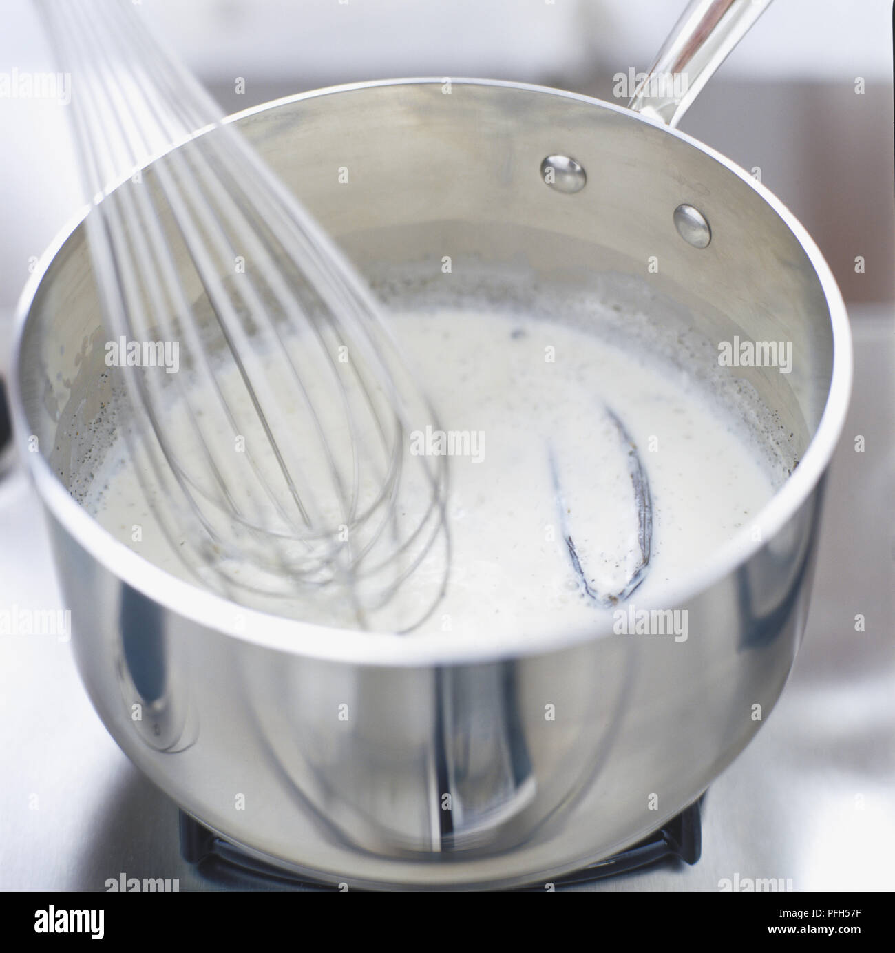 Metal whisk being used to stir milk and vanilla pods in saucepan ...