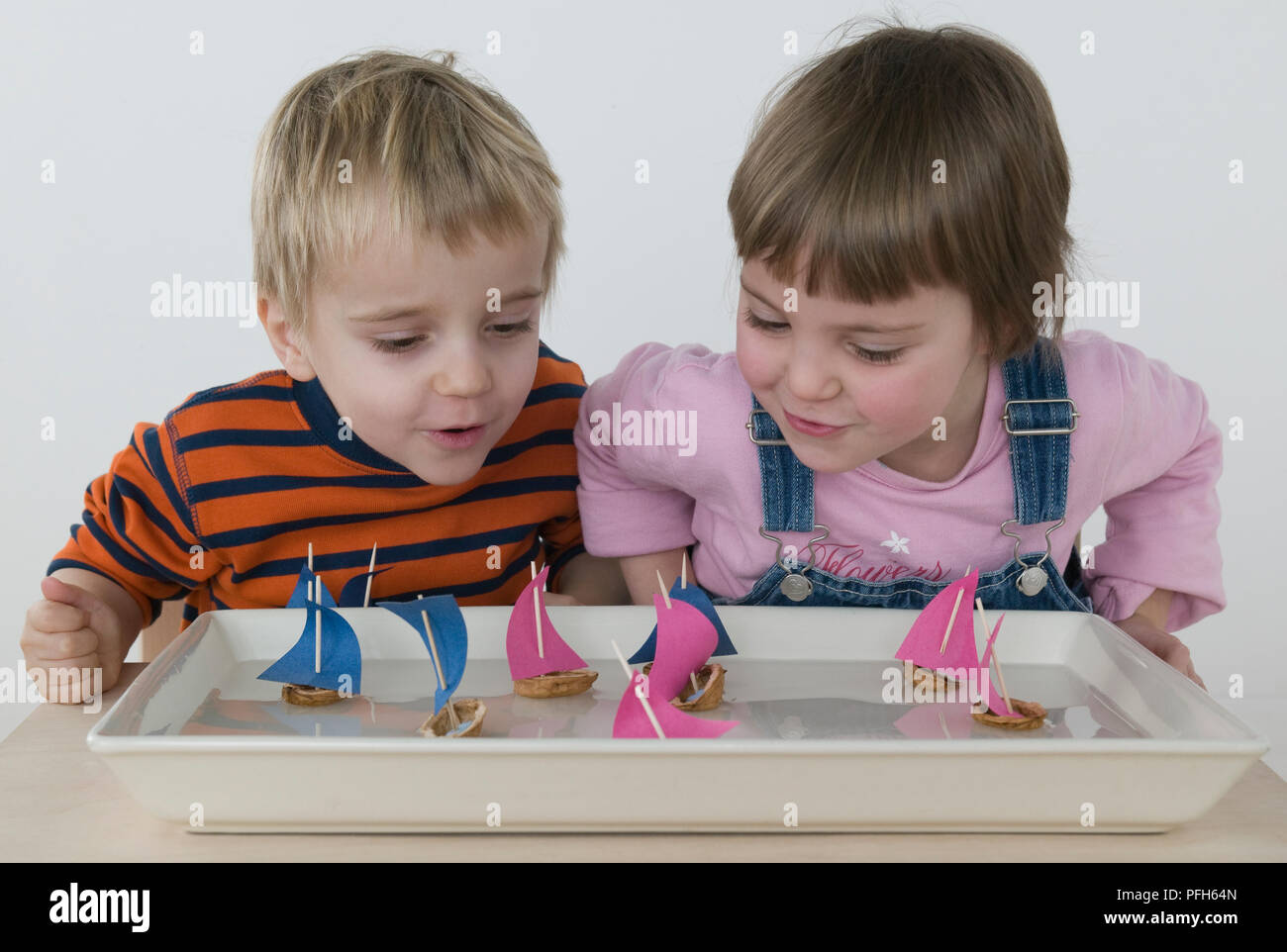 Boy and girl with toy sailing boats floating on water in tray Stock Photo