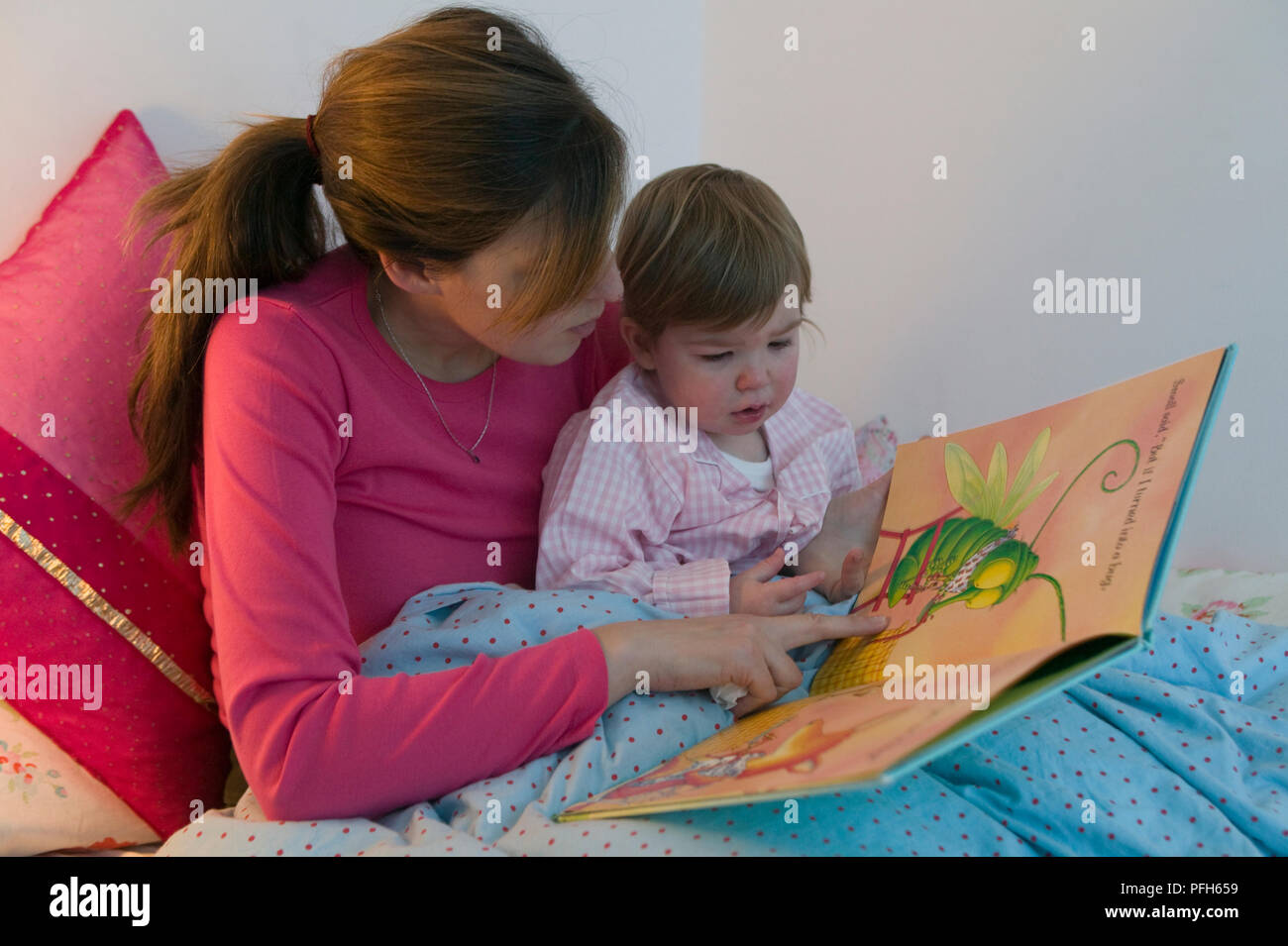 Woman and girl sitting in bed and looking at picture book Stock Photo ...