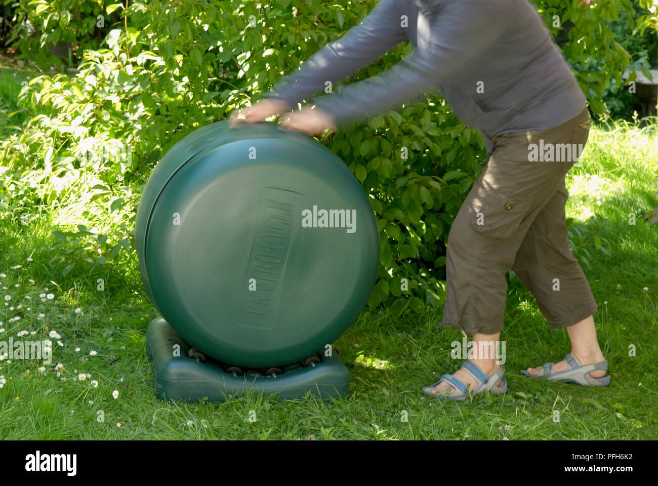 Woman turning green plastic compost tumbler bin, side view Stock Photo