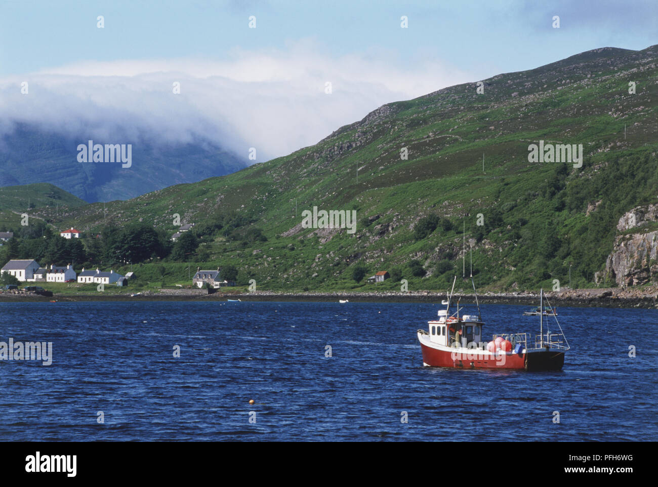 Great Britain, Scotland, red and white boat near mountainous coastline Stock Photo