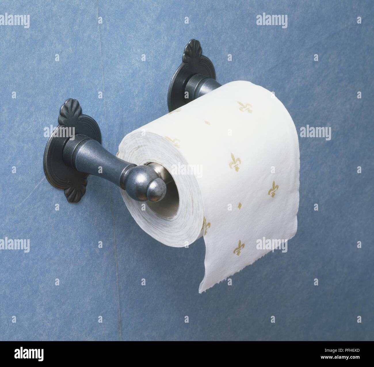 Roll of toilet paper showing fleur de lis pattern and ornate metal holder Stock Photo
