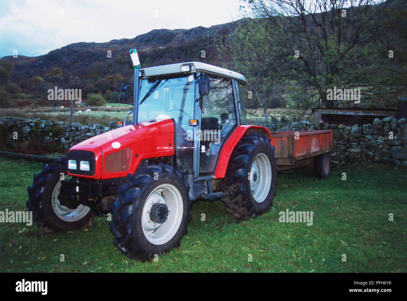 Red tractor parked by a stone wall Stock Photo
