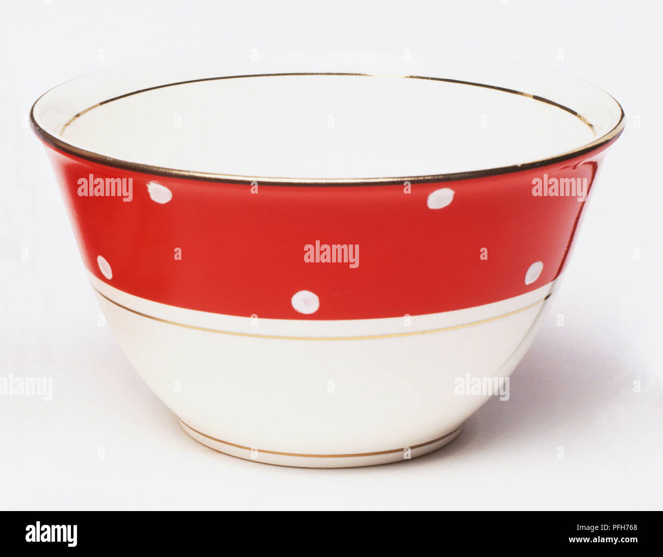 A red and white bowl, with a pattern of white dots and gold rim Stock Photo