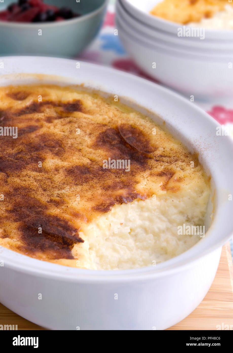 Rice pudding in ovenproof dish, bowls in background, closeup Stock