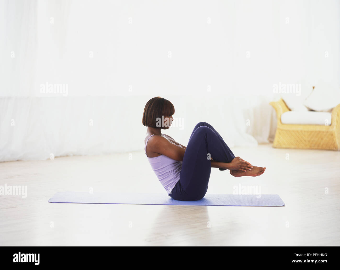 Woman sitting on an exercise mat, hands threaded through leg grasping