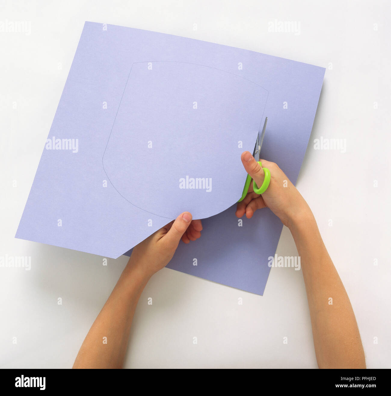 Cutting through purple card with green handled scissors. Stock Photo