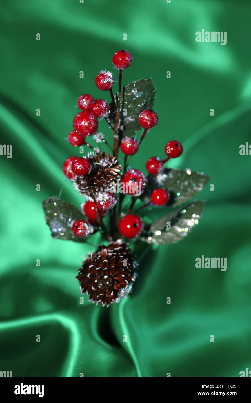 Christmas decoration of red berries, leaves, pinecones on green silk backdrop, close-up Stock Photo