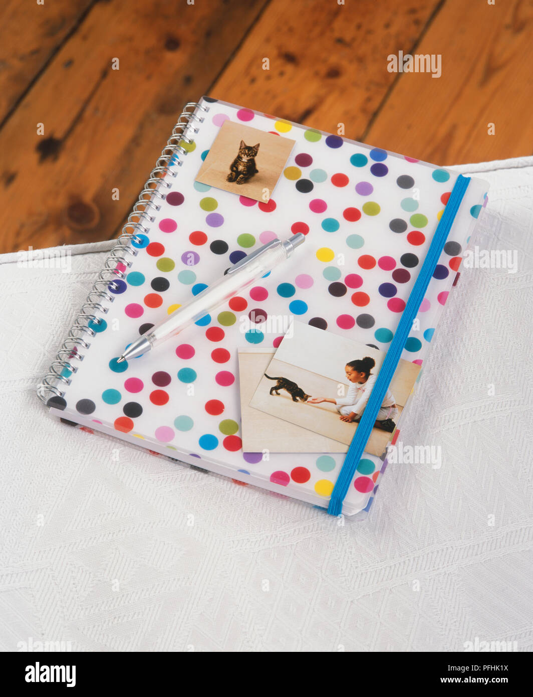 Ring bound journal with spotted patterned cover and elastic strap, photographs of girl and kitten, pen, view from above. Stock Photo