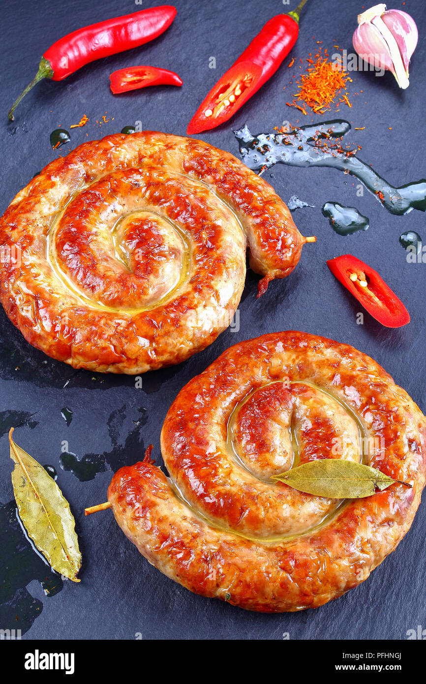 delicious hot bavarian Bratwurst - round fried sausages on wooden skewers on black slate plate with chili peppers and hot fat drops on background, ver Stock Photo