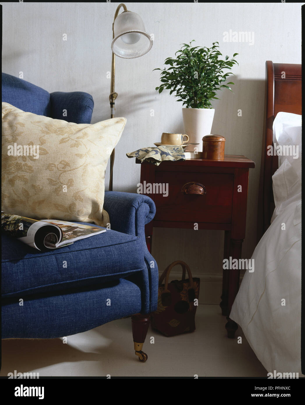 A Bedside cabinet with a flower on top with a bed and a chair either side Stock Photo
