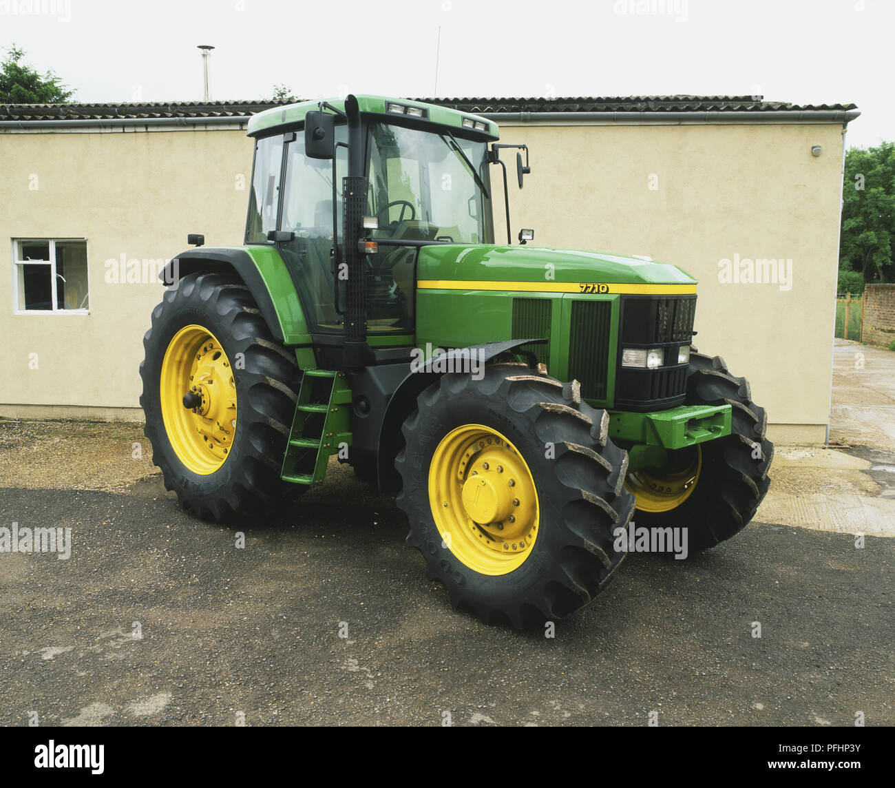 A green and yellow tractor parked outside a low building Stock Photo