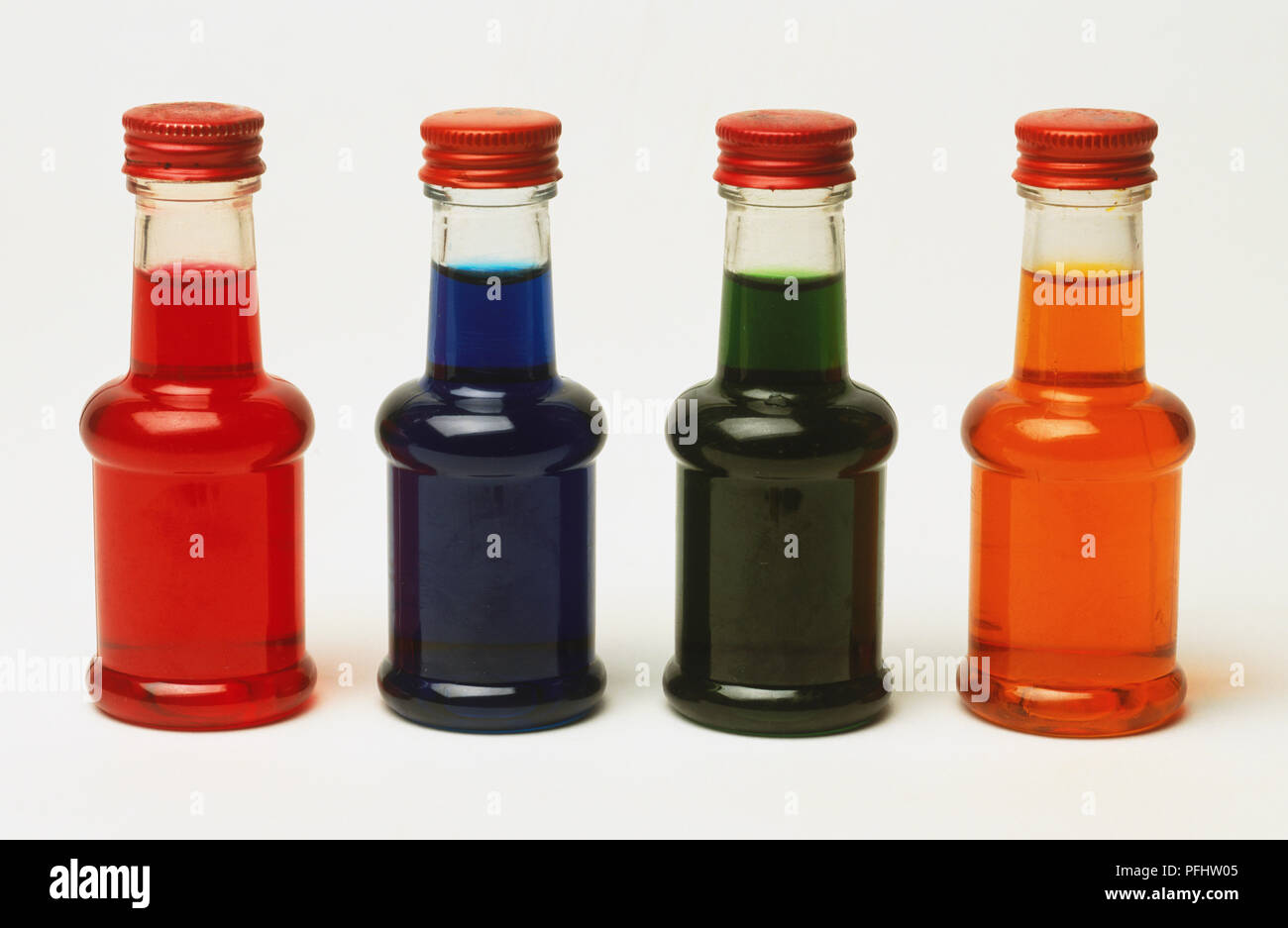 Four small plastic bottles containing coloured liquids, close up. Stock Photo