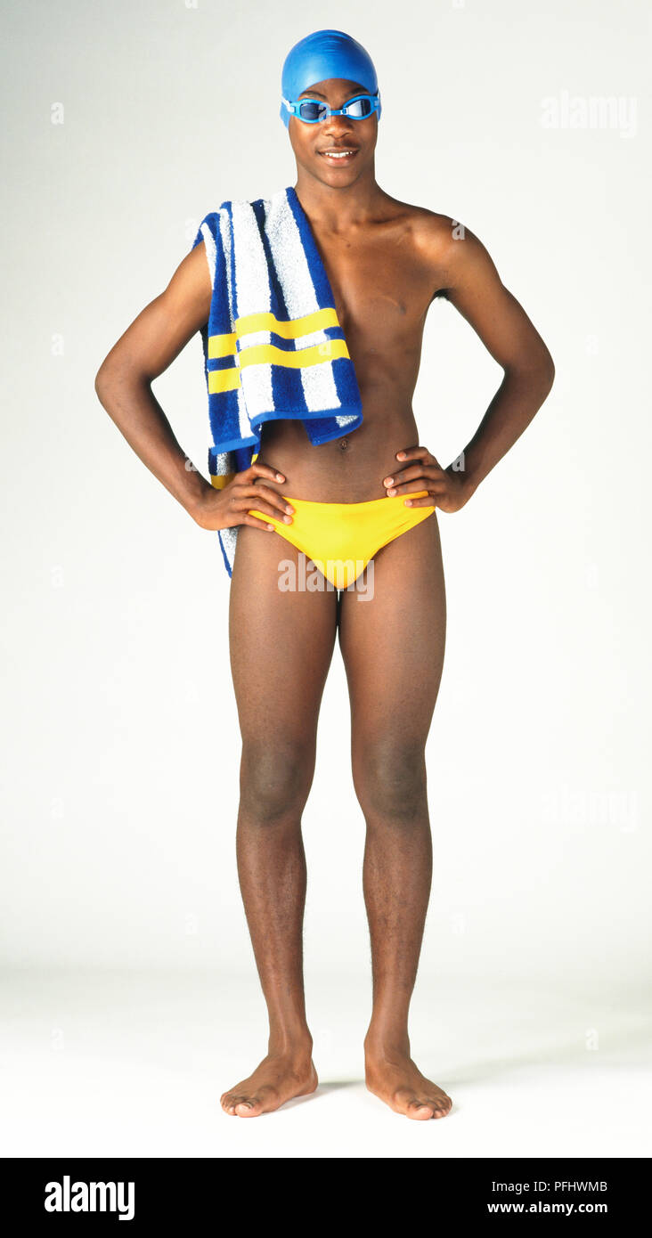 Teenage boy in yellow swimming trunks, goggles and blue cap, standing with  towel over his shoulder and hands on waist, front view Stock Photo - Alamy