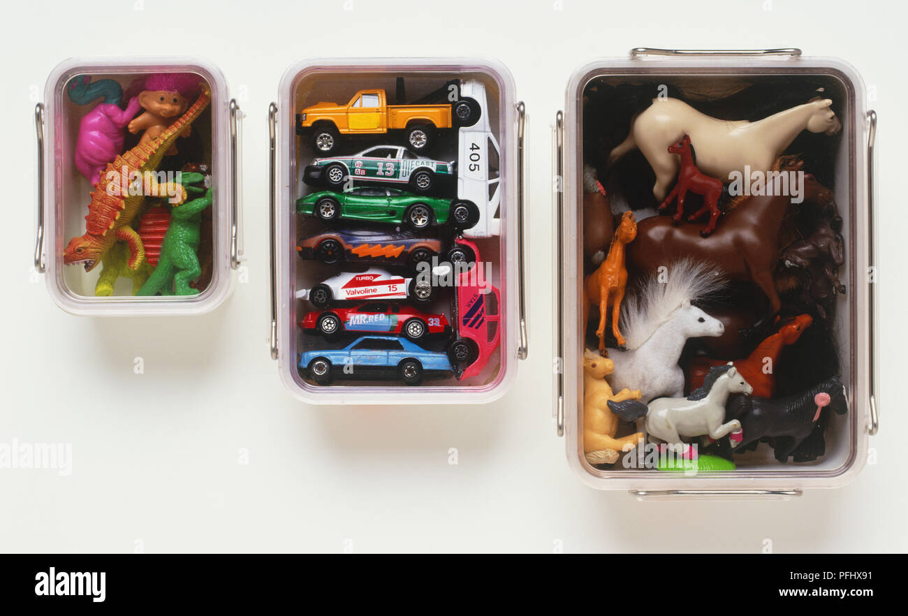 Three metal stacking boxes containing toy cars, miniature dinosaurs and miniature horses, view from above. Stock Photo