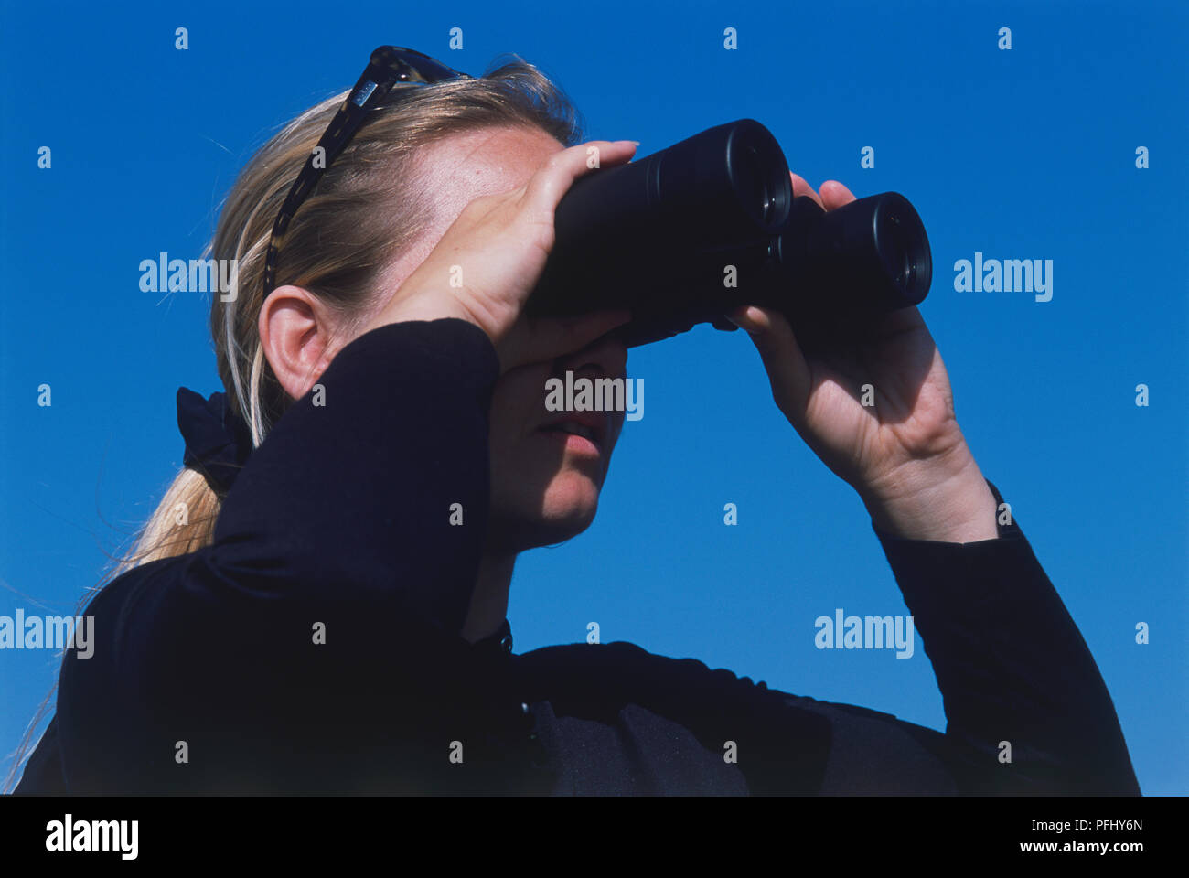 Blonde woman with sunglasses over her head looking into binoculars, low