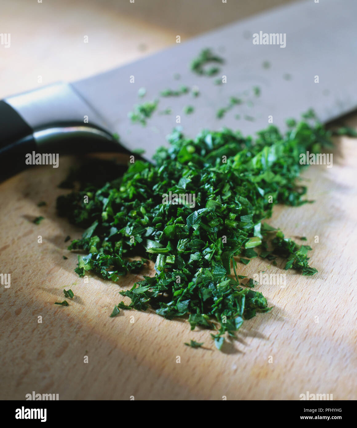 Petroselinum crispum, finely chopped Parsley leaves and a knife on a wooden board, close up. Stock Photo