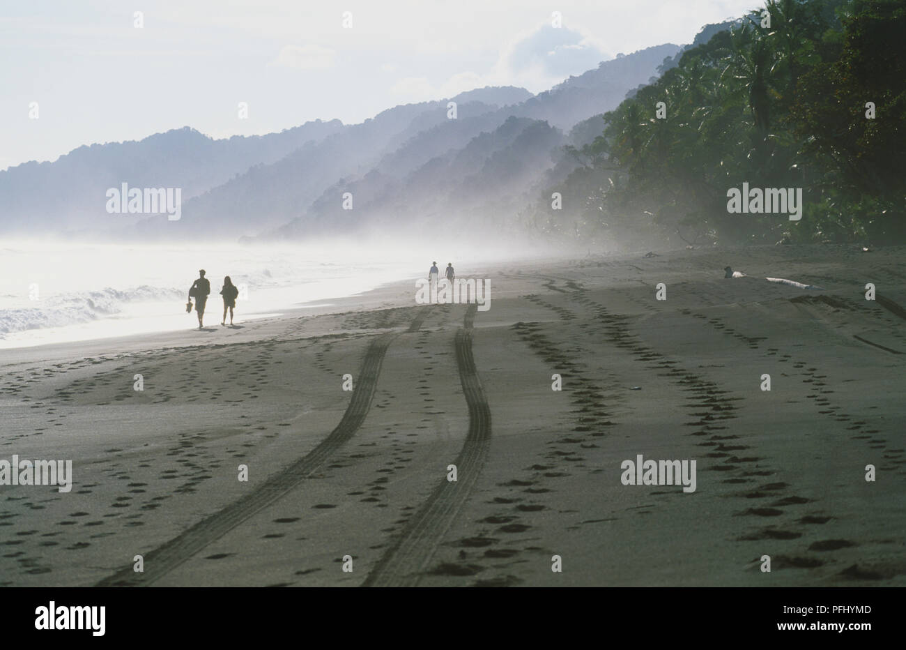 Central America, Costa Rica, Southern Zone, Peninsula de Osa, Parque Nacional Corcovado, couples walking, and waves crashing over wet sand beach indented with hoof prints and cart tracks on way from Carate in national park Stock Photo