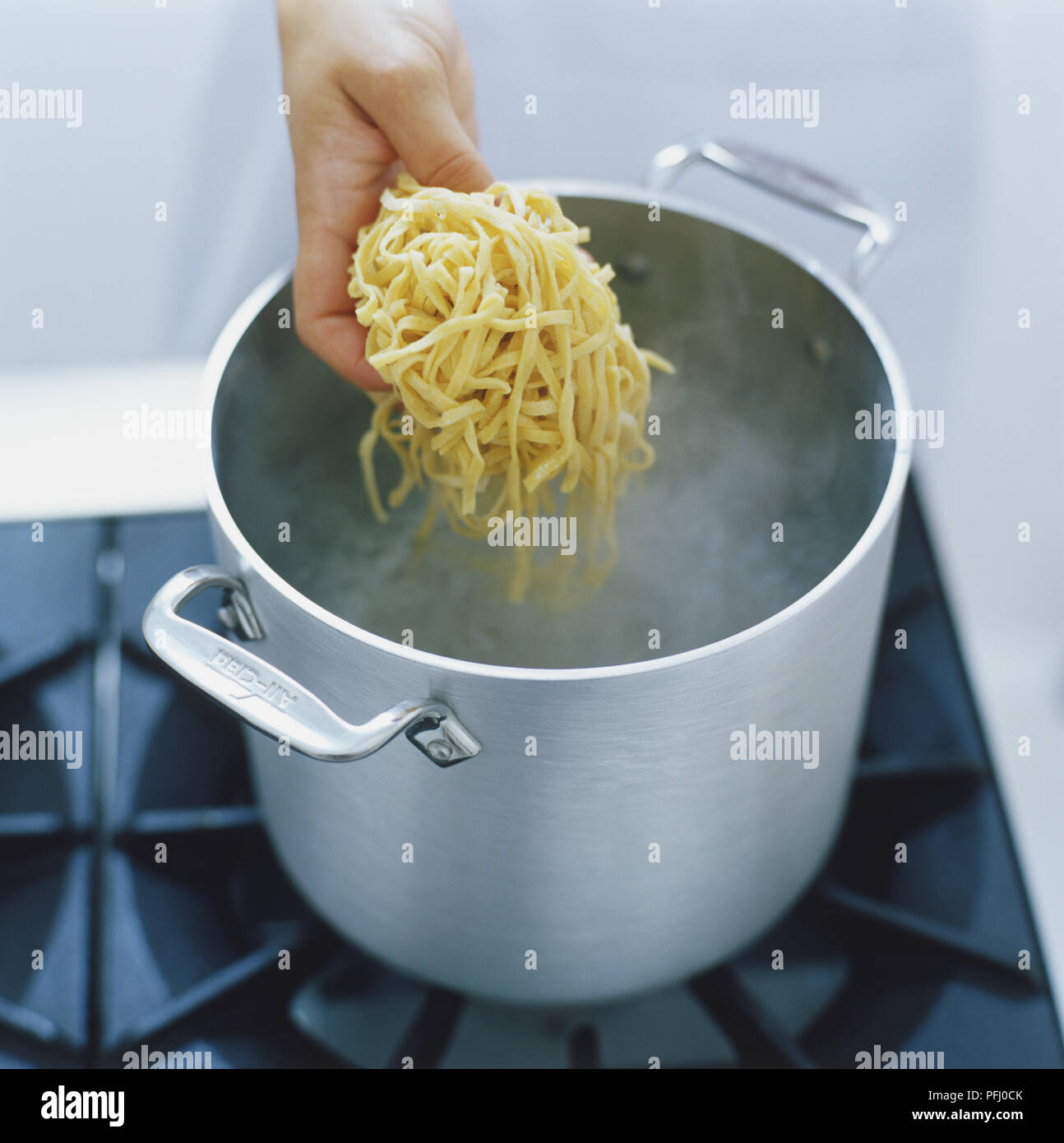 Ball of fresh pasta strands being lowered into steaming saucepan, high ...