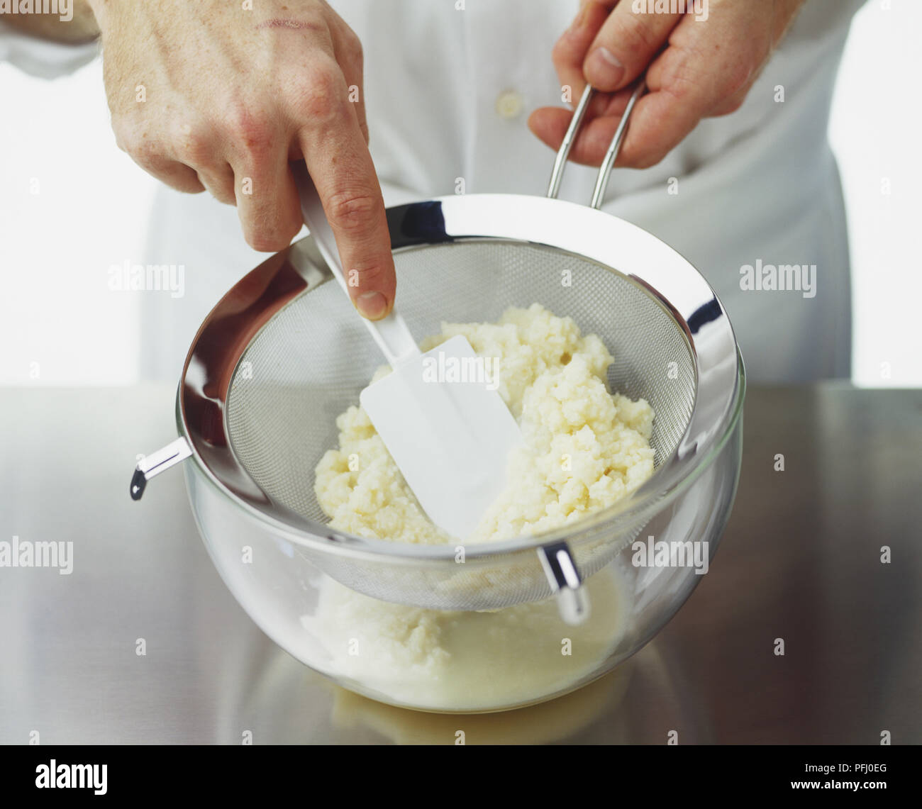Celeriac puree being pressed through sieve with rubber spatula, high angle view Stock Photo