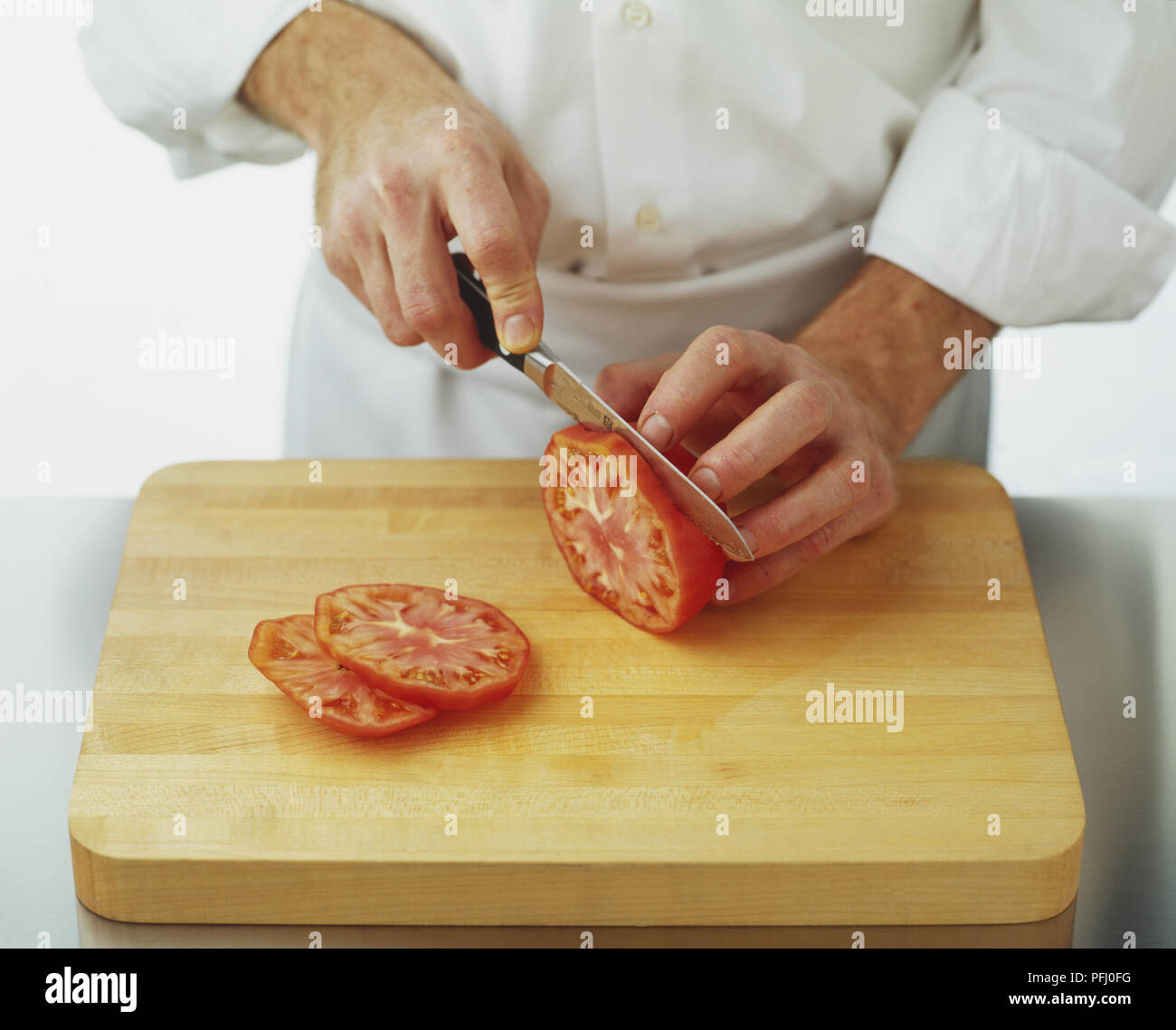 Using a serrated knife to cut tomato into slices Stock Photo Alamy
