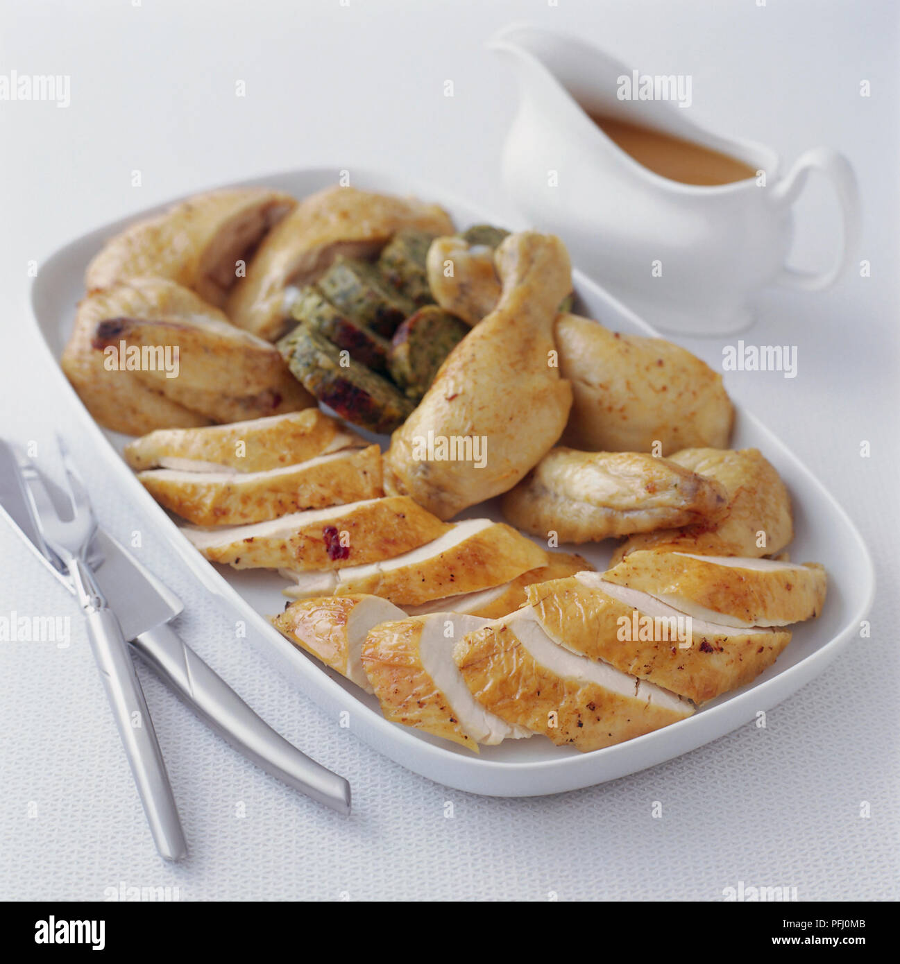 Platter of various sliced poultry and drumsticks, and a gravy boat Stock Photo
