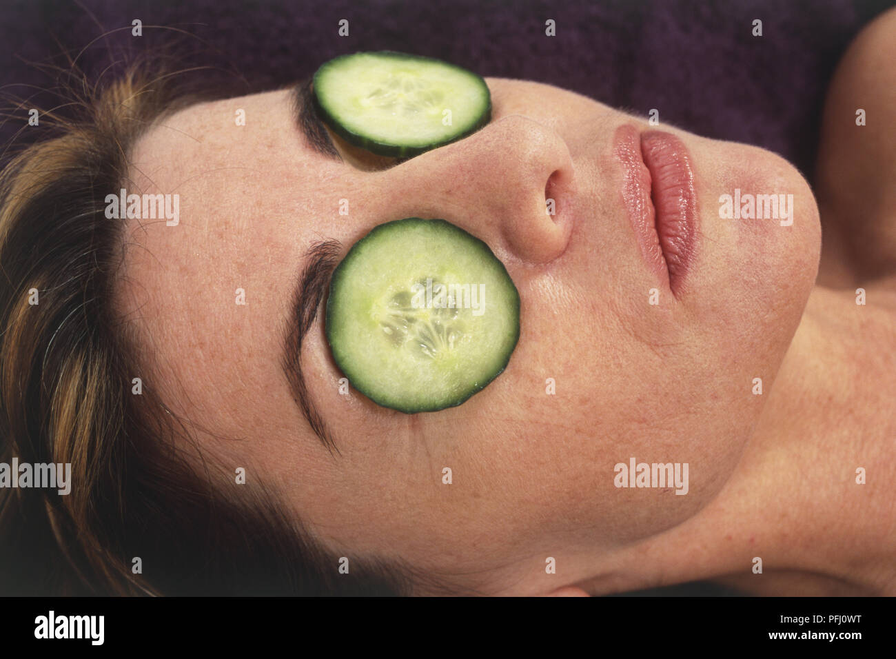 Woman lying down with cucumber slices on each eye. Stock Photo