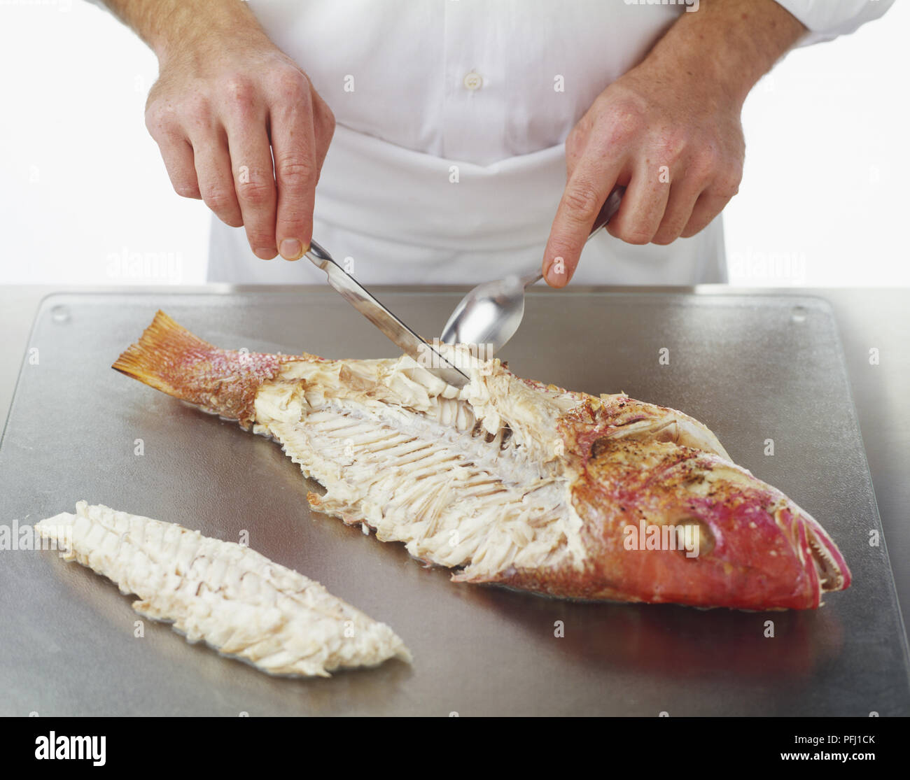 Using a spoon and a knife to remove fillets from a cooked Red Snapper Stock Photo
