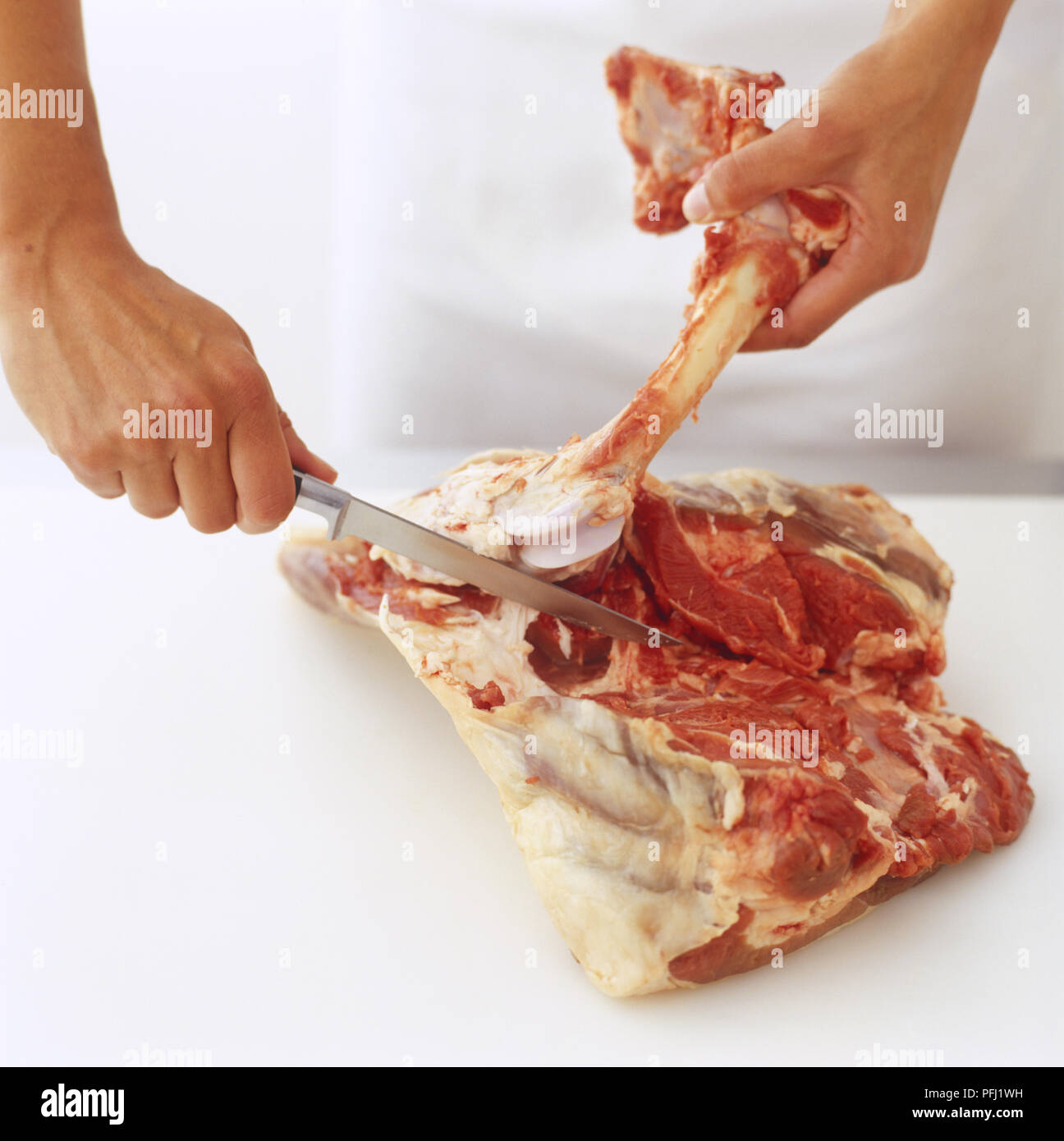 Using knife and hands to pull away bone from a leg of lamb Stock Photo